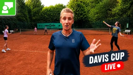 Coach on a red clay tennis court speaks to the camera; players practice in the background; 'Davis Cup Live' banner overlaying the image.